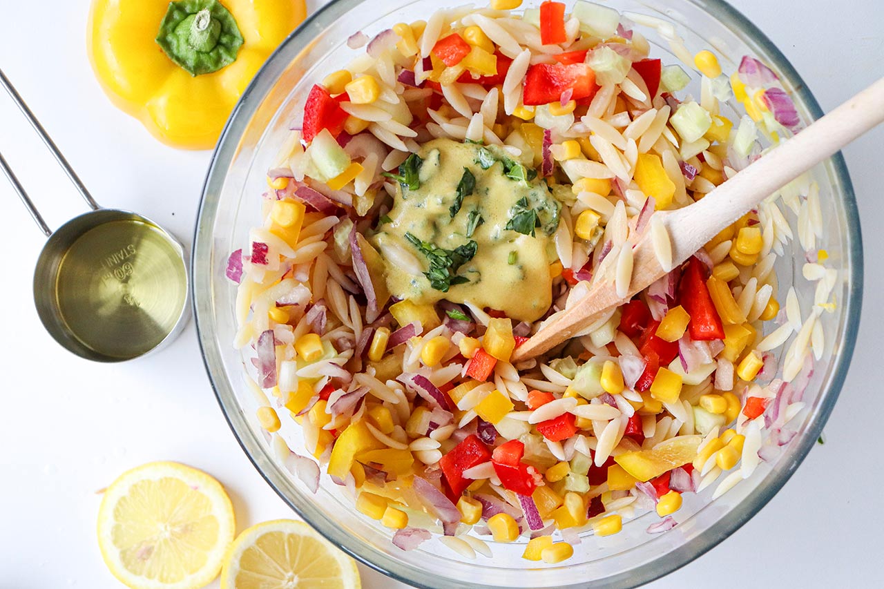 Dressing added to a bowl of orzo salad.
