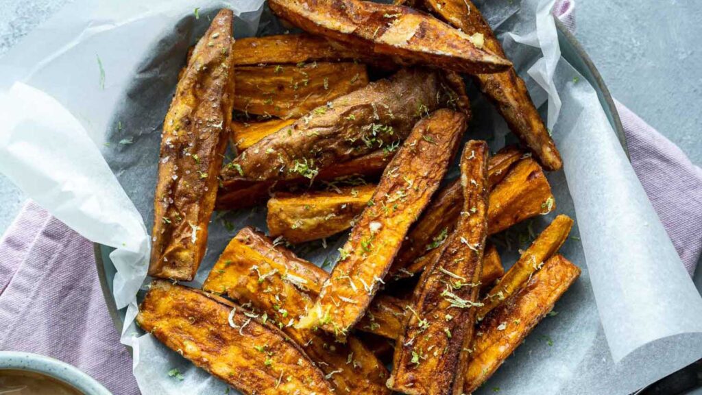 Sweet potato wedges in a parchment-lined, shallow bowl. Overhead focus.
