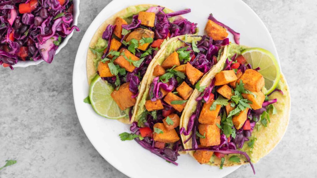 A white plate holds three sweet potato tacos. Overhead focus.