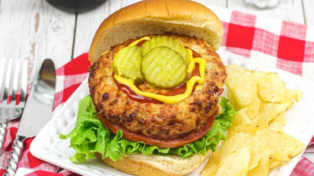An open-faced air fryer chicken burger with ketchup, mustard, and pickle slices.