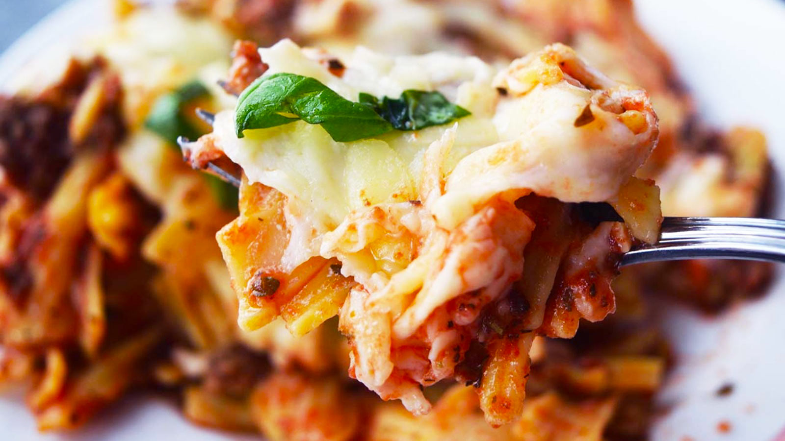 A fork hold a bit of baked ziti over a plateful.