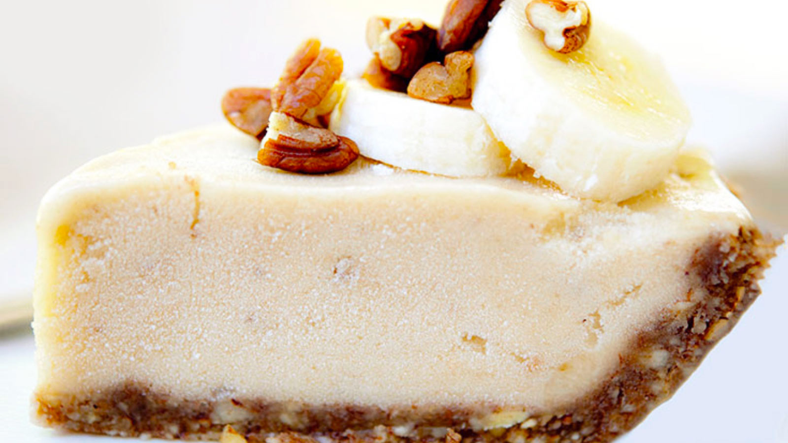 A slice of Ice Cream Pie from the side shows a nice thick layer of filling with sliced bananas and pecan pieces on top. White background.