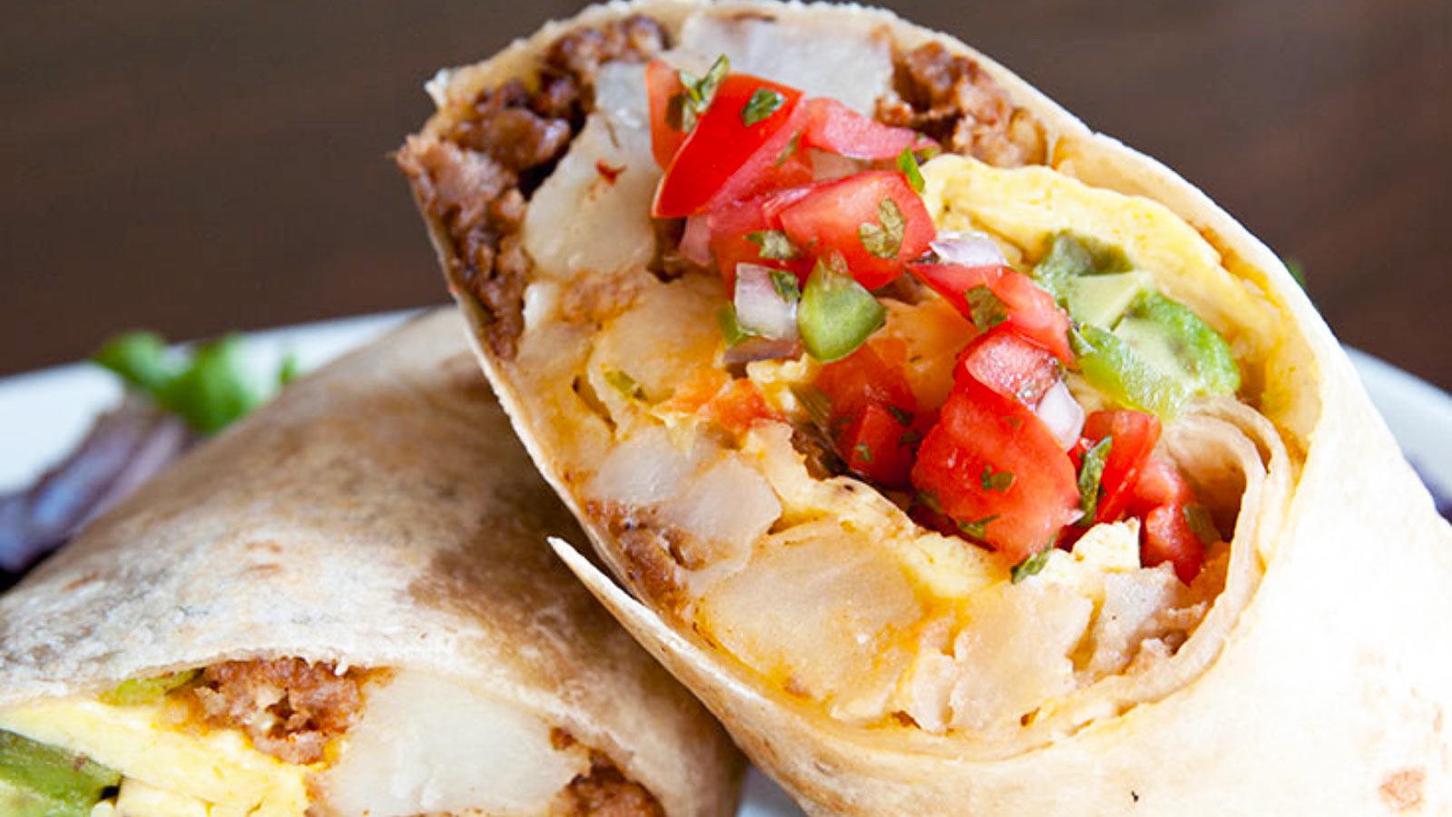 A cut breakfast burrito up close, showing all the fillings.