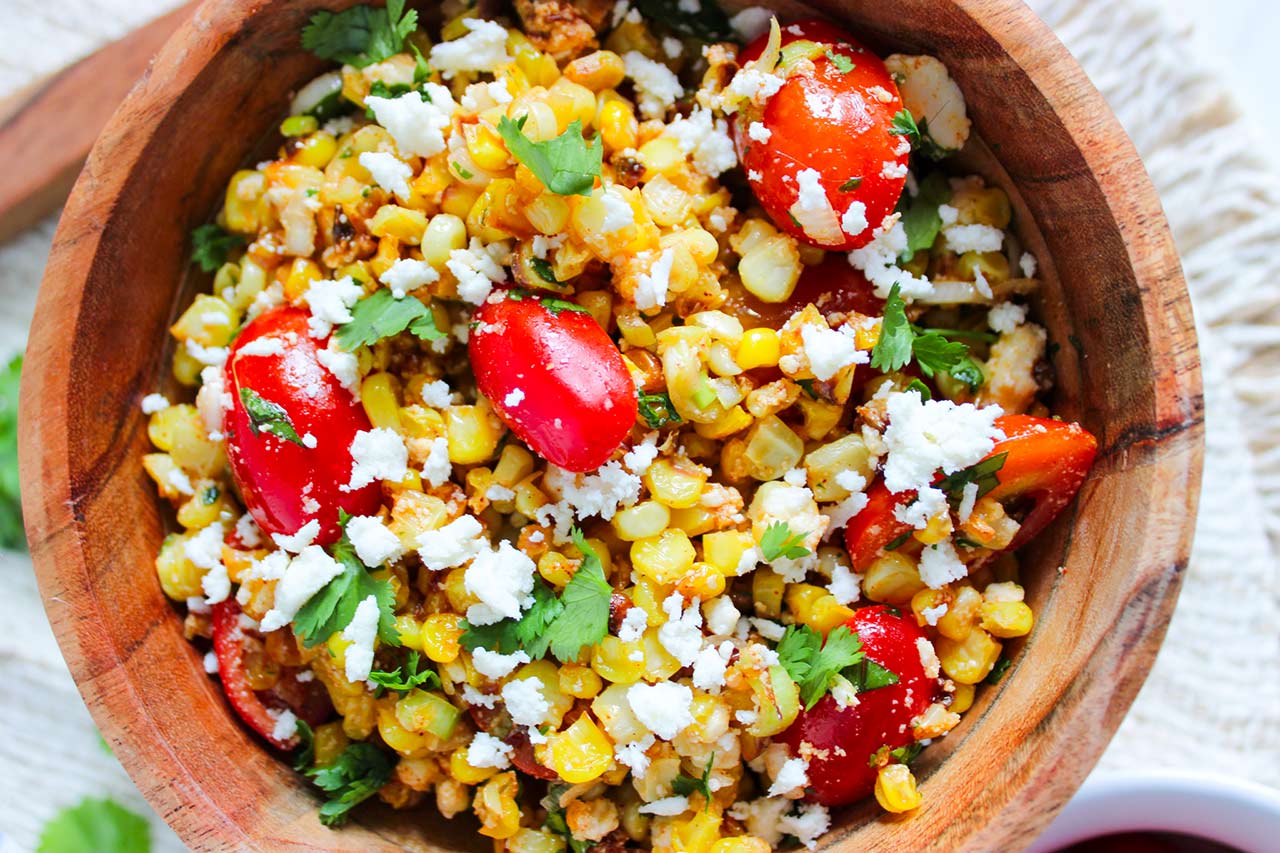 An overhead view of a wood serving bowl filled with Roasted Corn Salad.