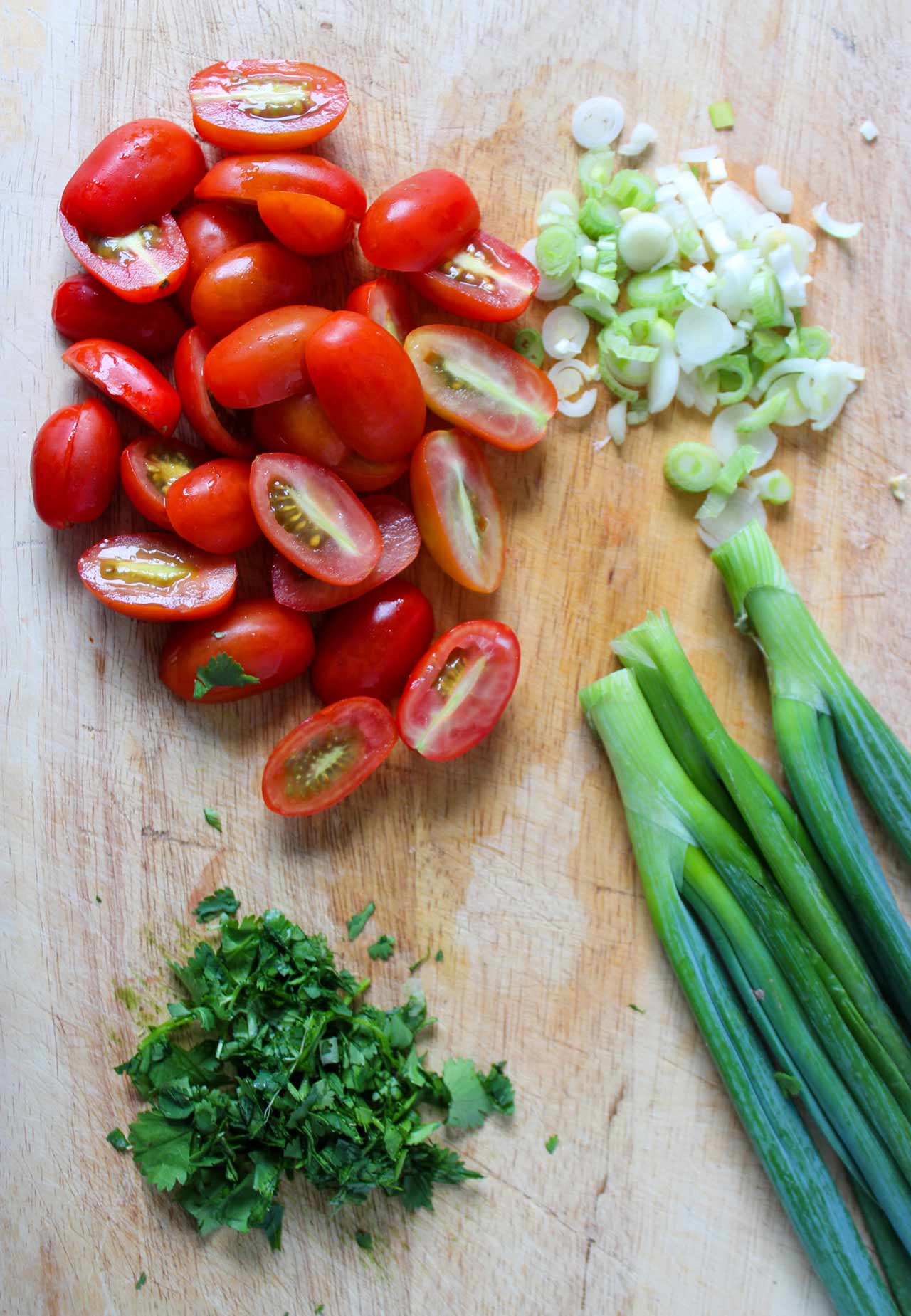 Chopped green onions, tomatoes, and cilantro chopped and sliced on a cutting board.