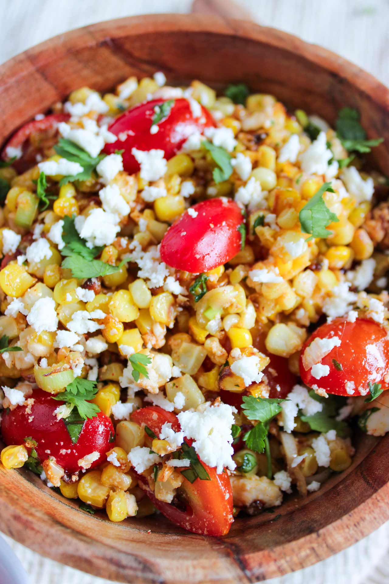 A side view of a wood bowl filled with Roasted Corn Salad.