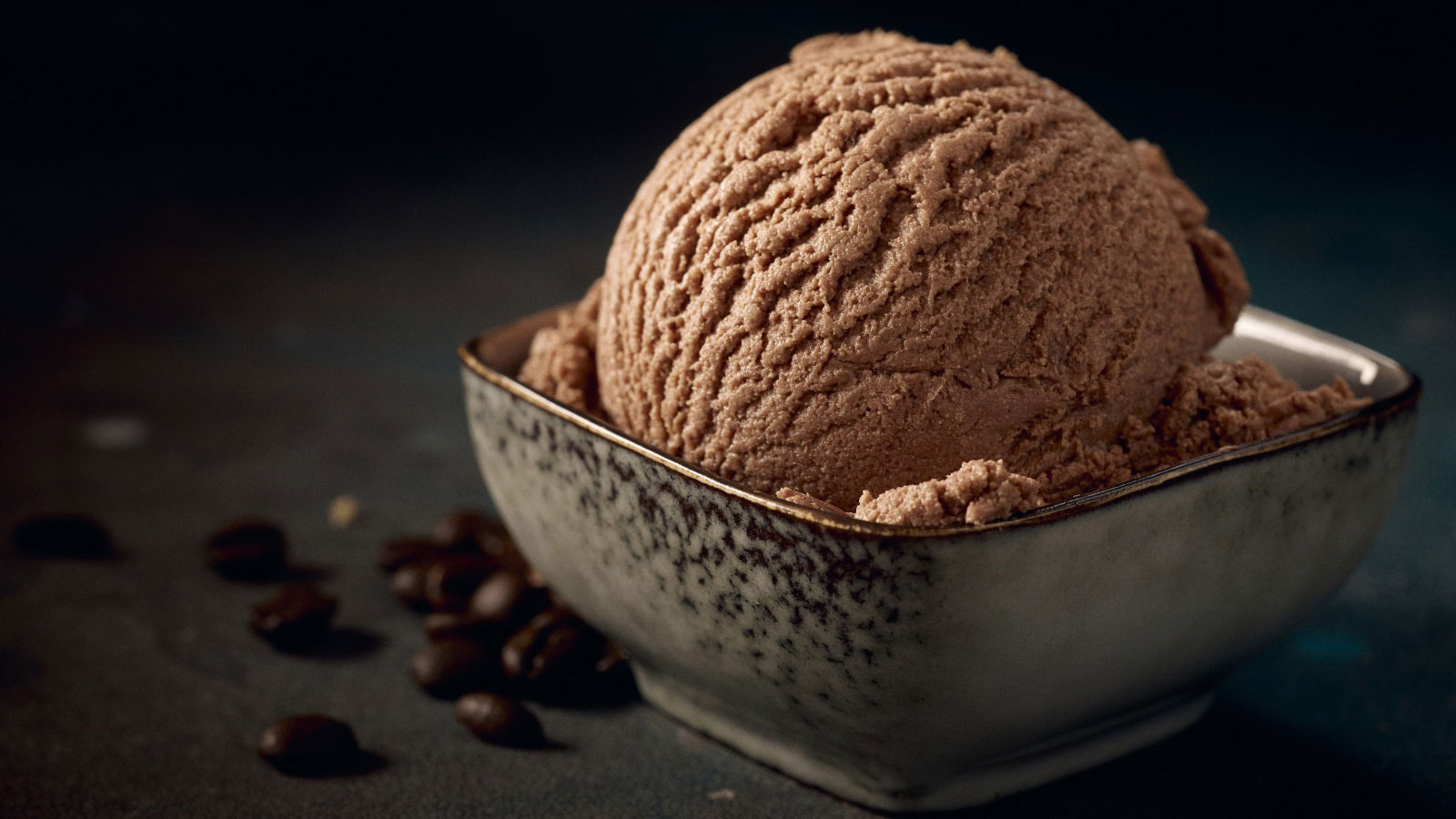 Scoop of tasty chocolate ice cream with creamy texture in square shaped bowl on table on a dark background.
