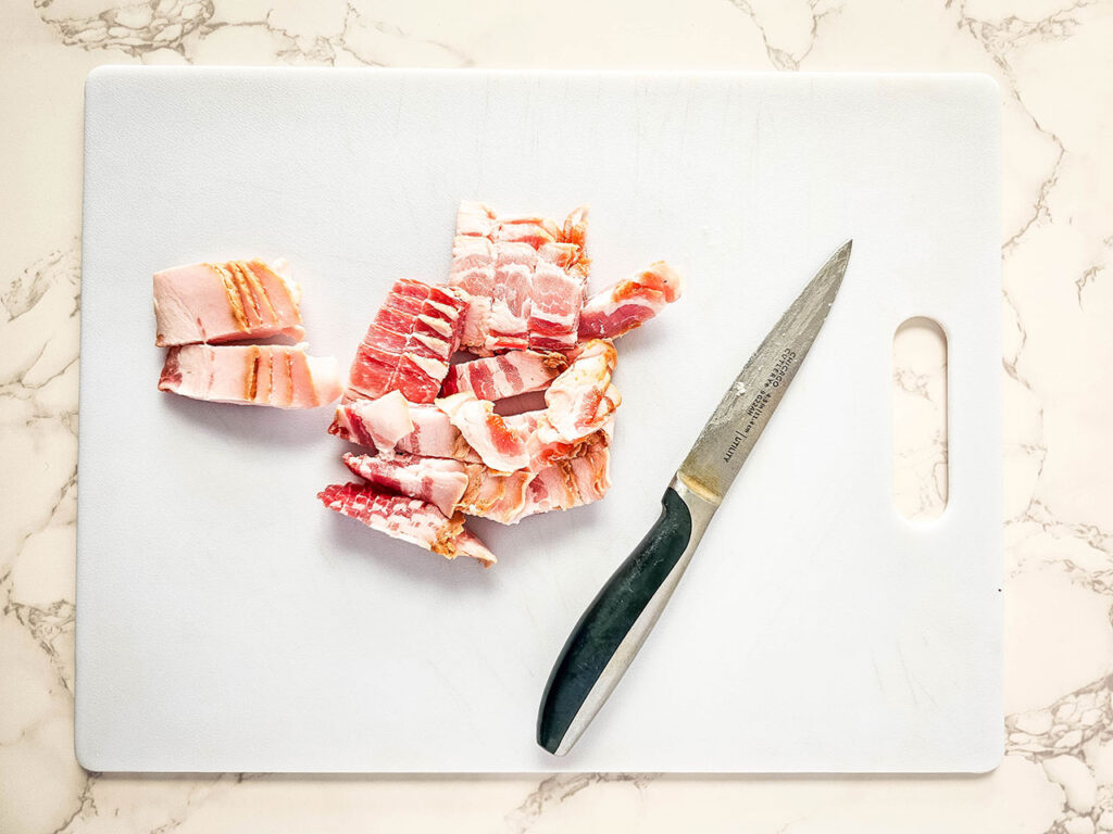Bacon slices cut into small pieces on a white cutting board.