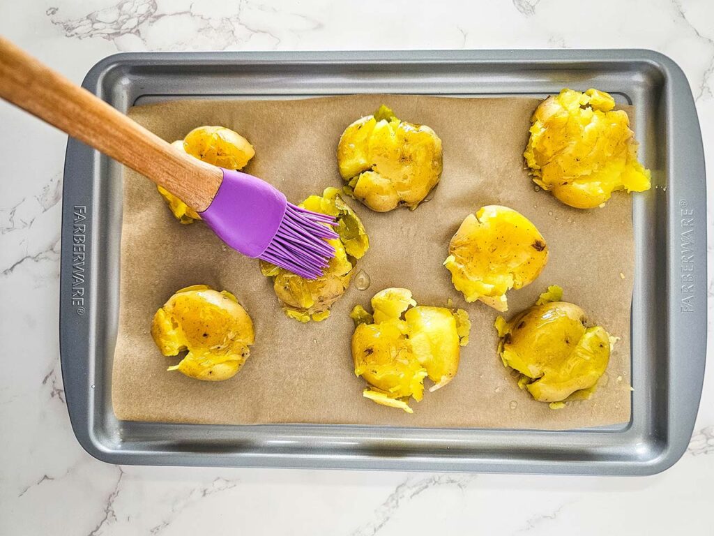 Basting smashed potatoes with oil on a sheet pan.