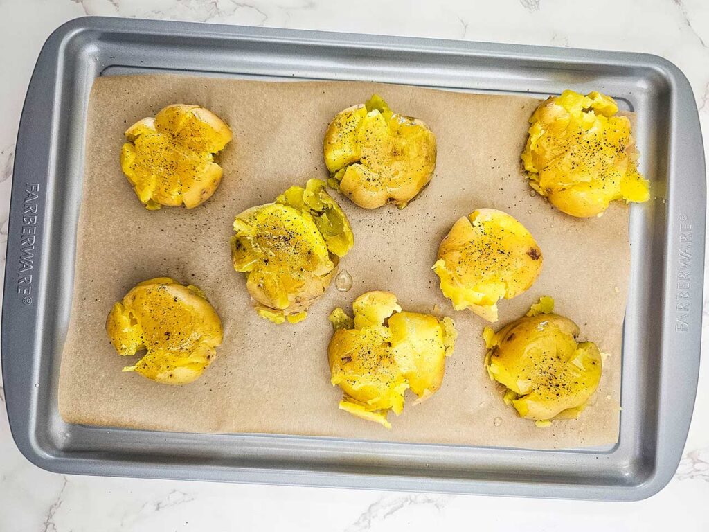 Smashed potatoes on a sheet pan sprinkled with pepper.