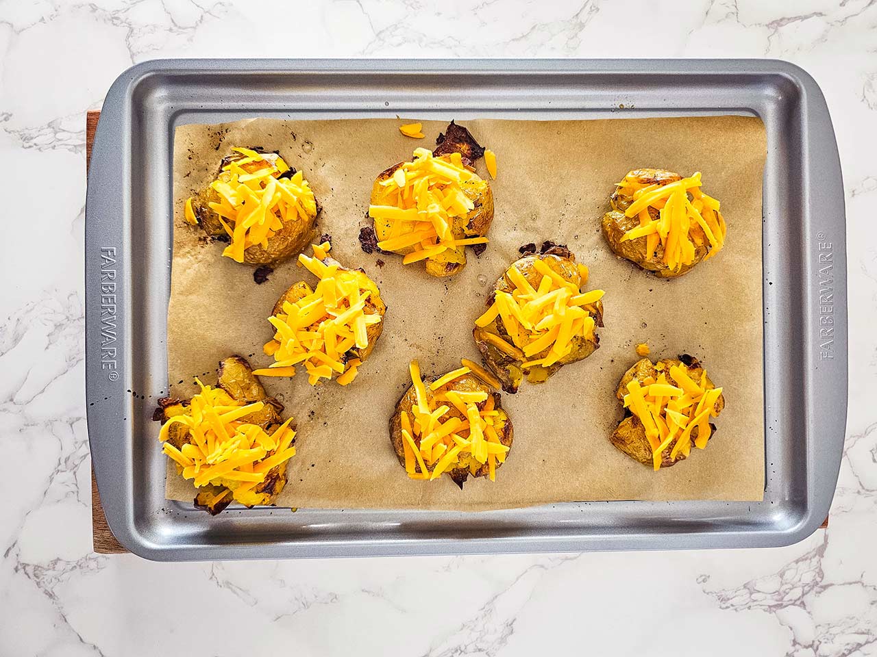 Smashed potatoes on a sheet pan sprinkled with grated cheese.