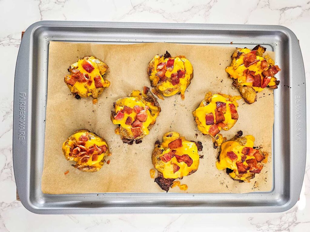 Smashed potatoes on a baking sheet sprinkled with bacon bigs over melted cheese.