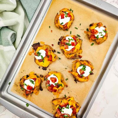 An overhead view of loaded smashed potatoes on a sheet pan.