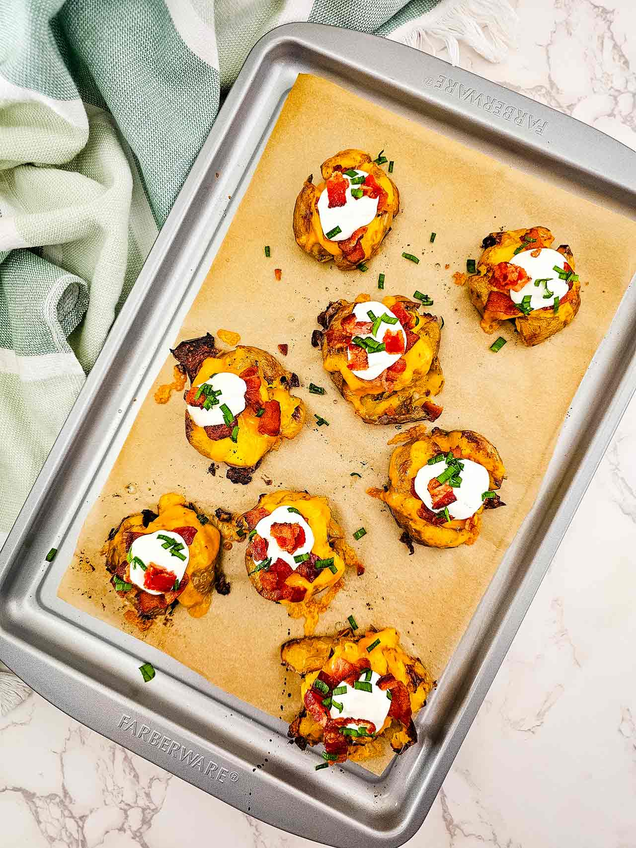 An overhead view of loaded smashed potatoes on a sheet pan.