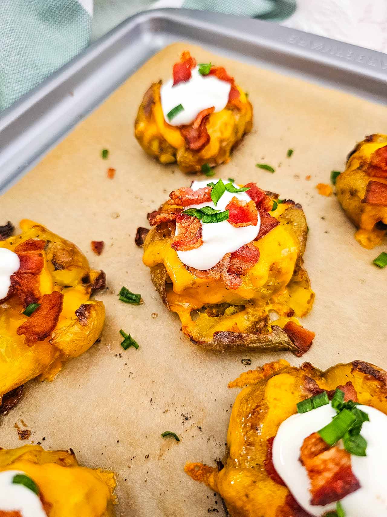 A close up of loaded smashed potatoes on a sheet pan.