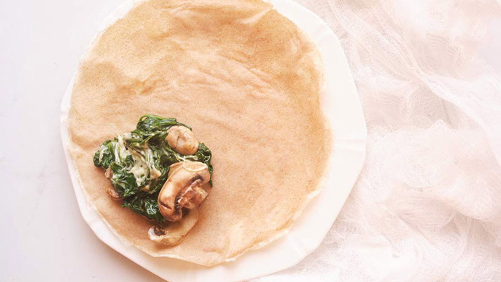 An overhead view of a crepe with savory mushroom and spinach filling.
