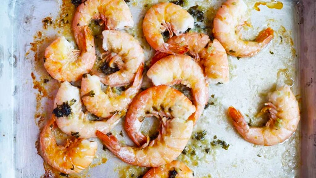 Sheet pan garlic shrimp laying on a baking pan smothered in butter and parsley.