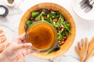 A hand holds a glass bowl of dressing over a bowl of Southwest Salad.