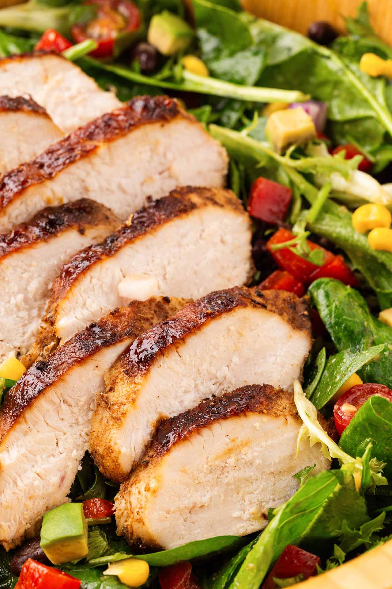 A closeup of chicken breast slices served over a Southwest Salad in a wood serving bowl.