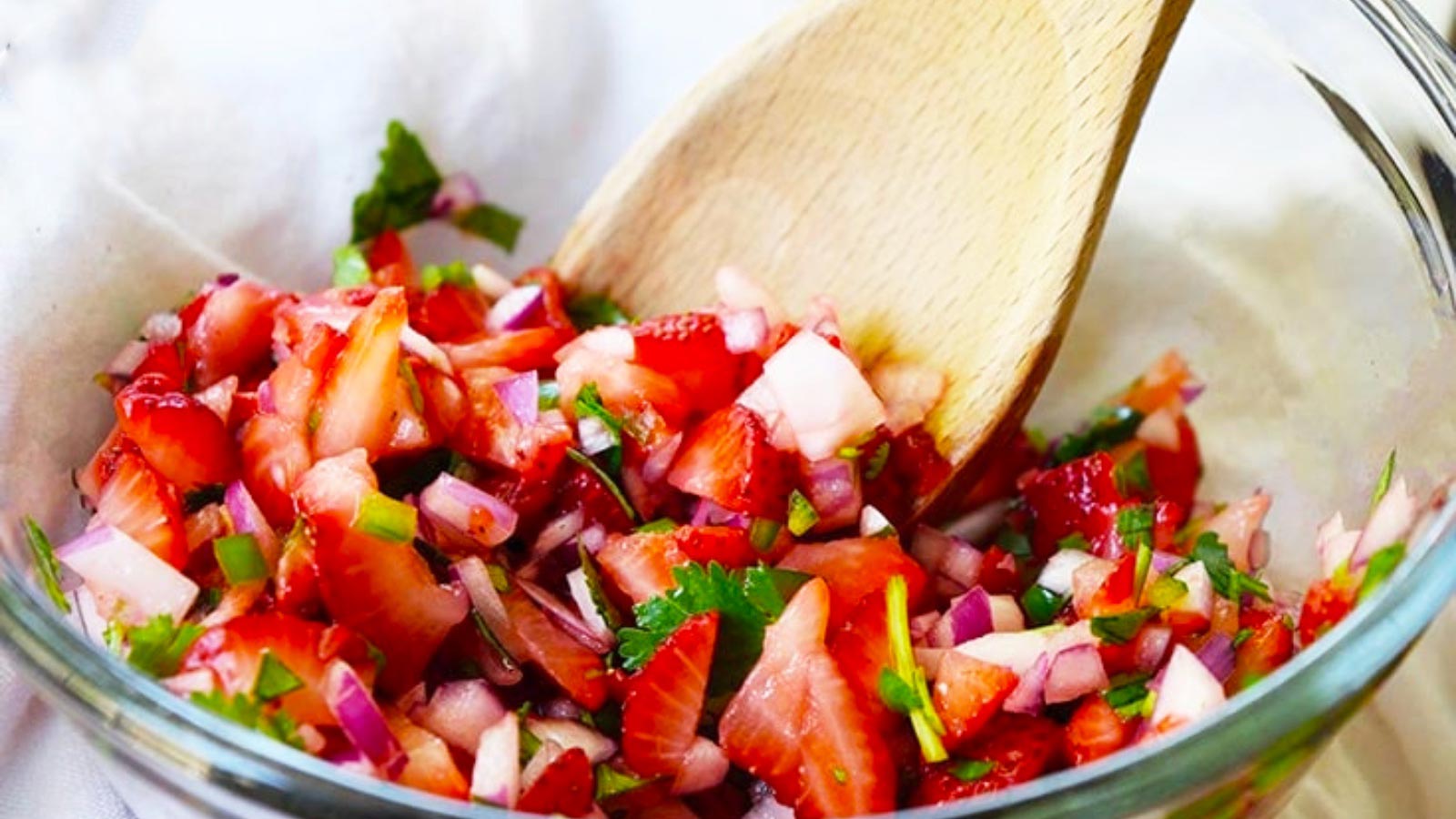 A glass bowl holds just-made strawberry salsa. A wooden spoon rests in the bowl.