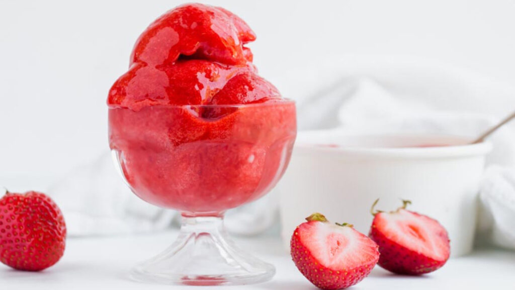 A glass ice cream bowl filled with Strawberry Sorbet on a white surface.