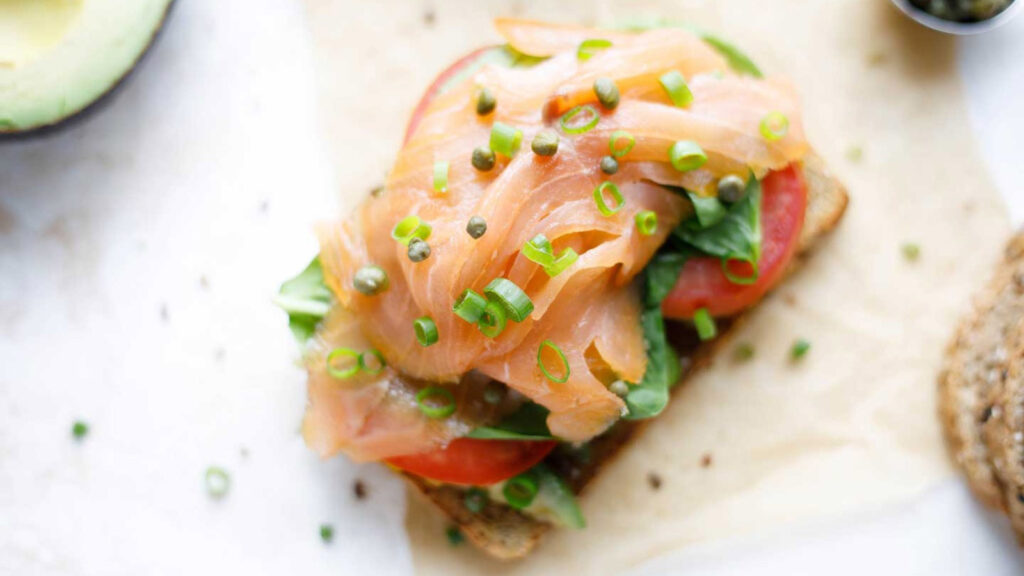 A single slice of smoked salmon avocado toast sitting on some parchment.