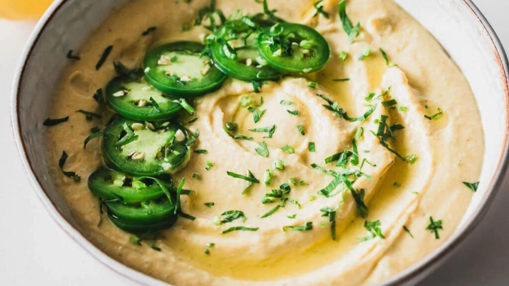 A bowl of hummus with slices of jalapeno arranged ontop.