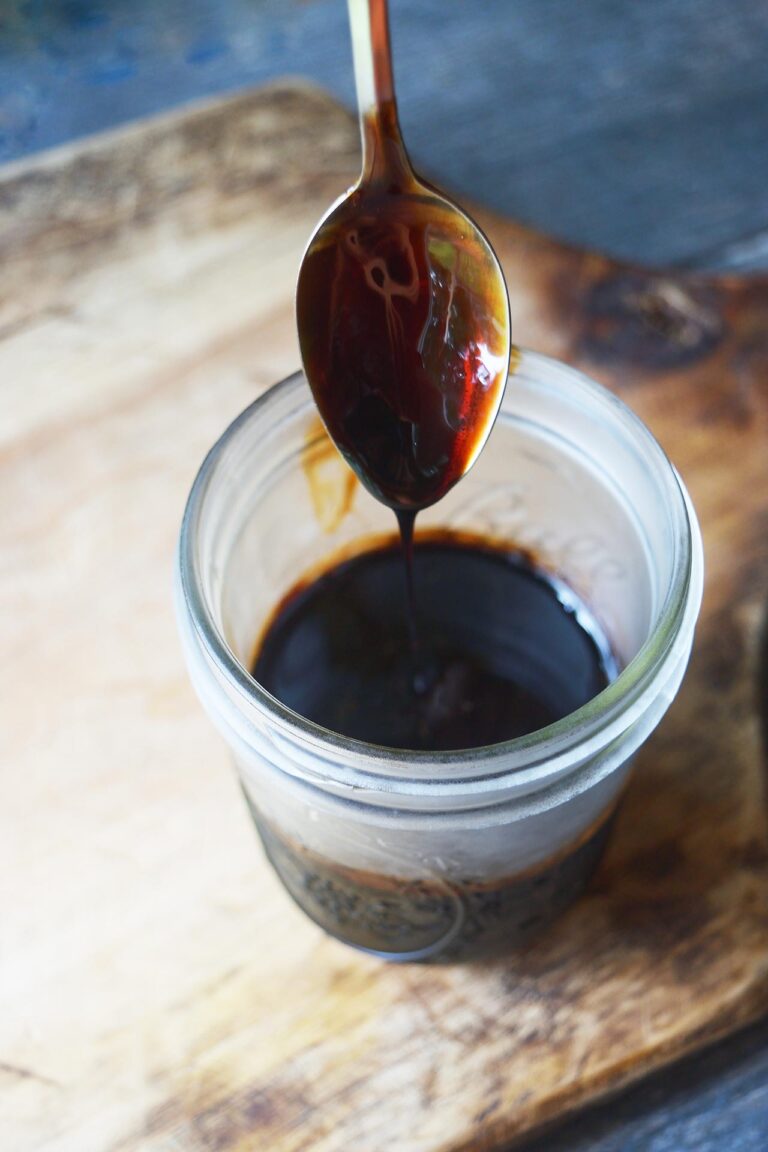 Drizzling balsamic glaze off a spoon into an open jar.