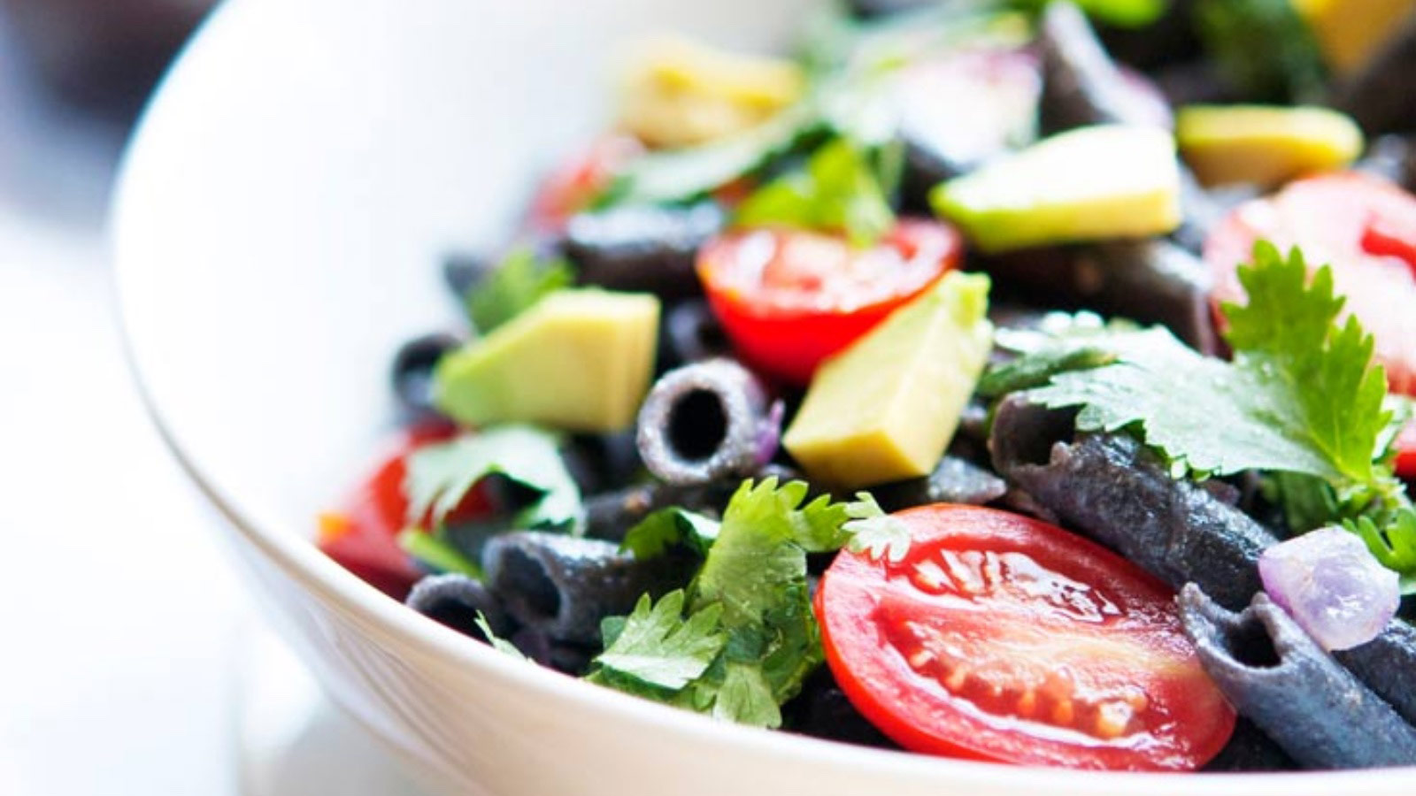 Closeup of a white bowl filled with black bean pasta salad.