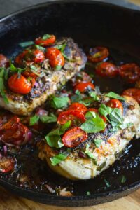 Two chicken breasts with bruschetta topping in a cast iron skillet.