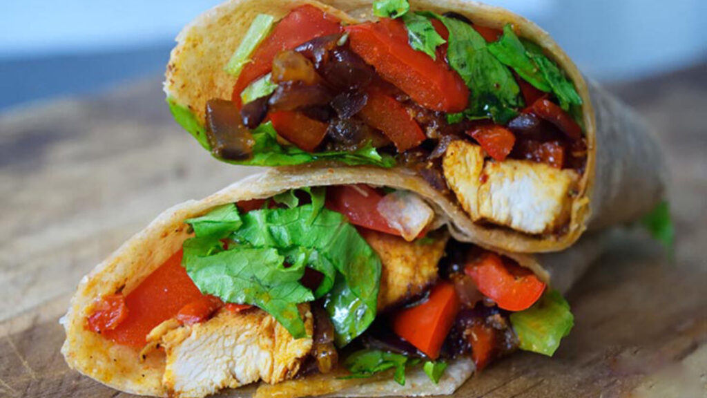 A cut Cajun Chicken Wrap sitting stacked on a cutting board.