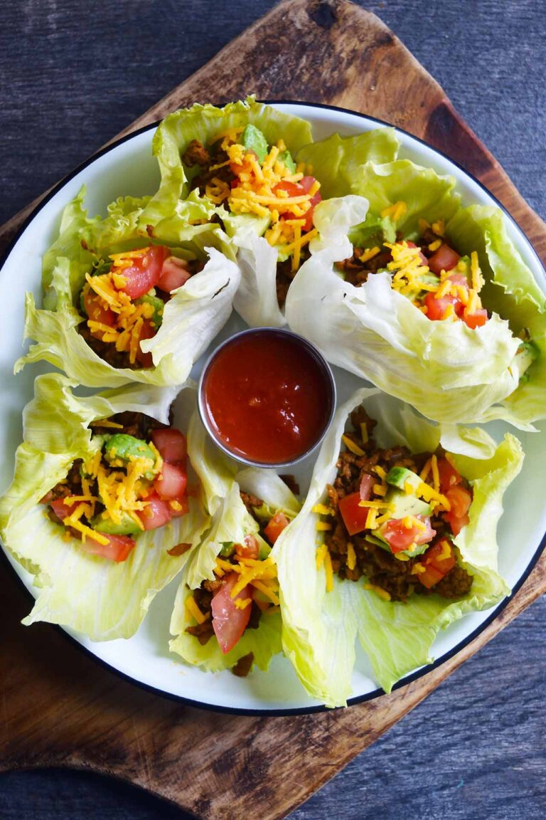A white platter of Taco Lettuce Wraps sits on a wood cutting board on a slate surface.