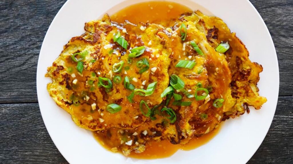 An overhead view of a white plate holding 4 egg foo young pancakes which are drenched in sauce and garnished with fresh, sliced, green onions.