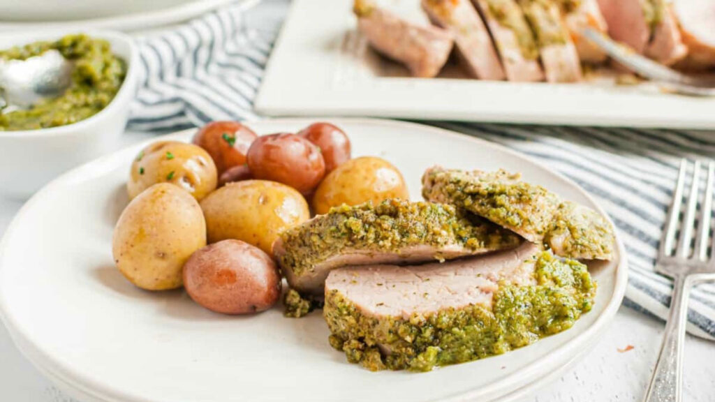 Slices of pesto pork on a place with baby potatoes.