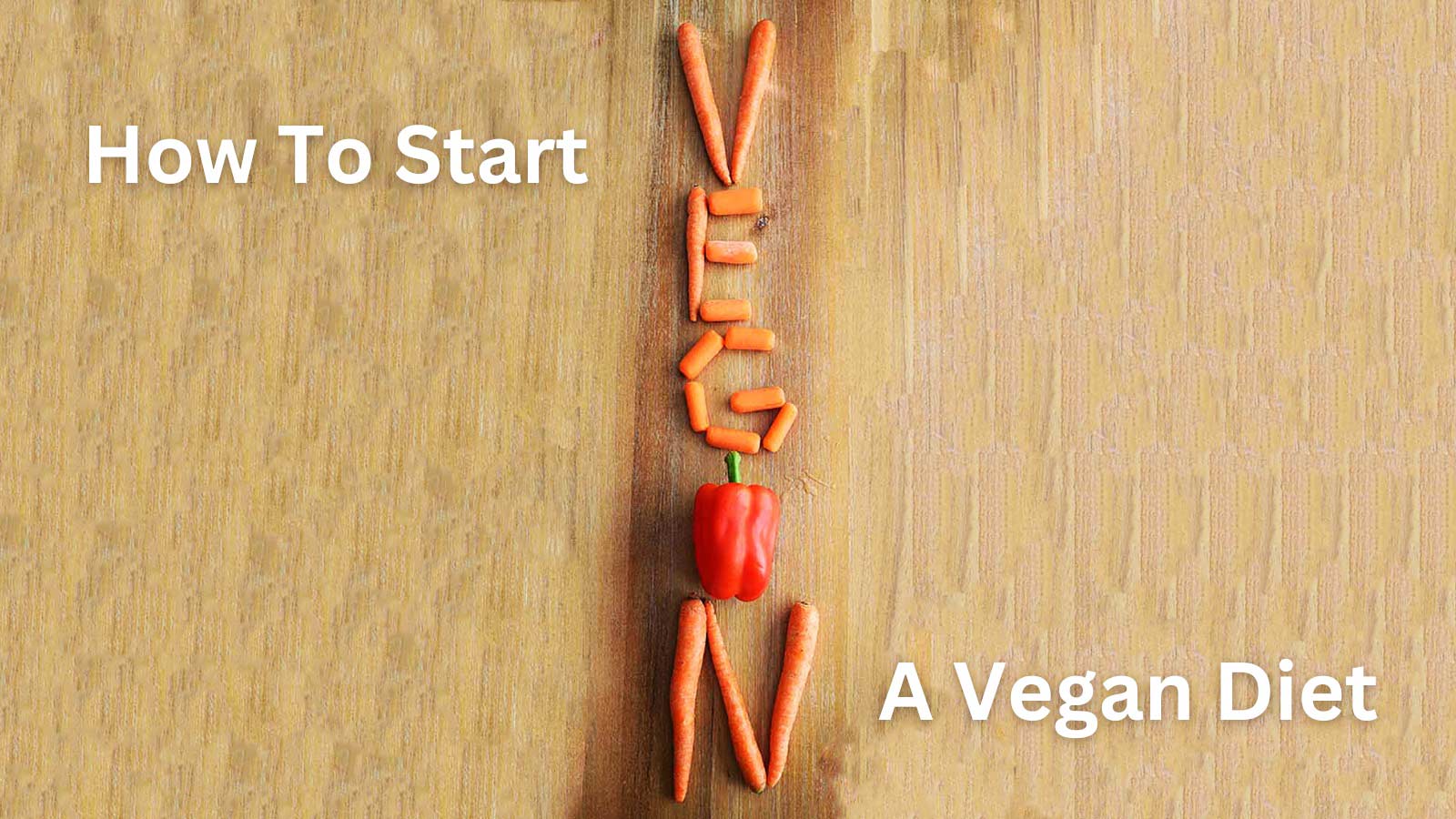 Carrots and a red bell pepper arranged on a wooden surface to spell the word, vegan.