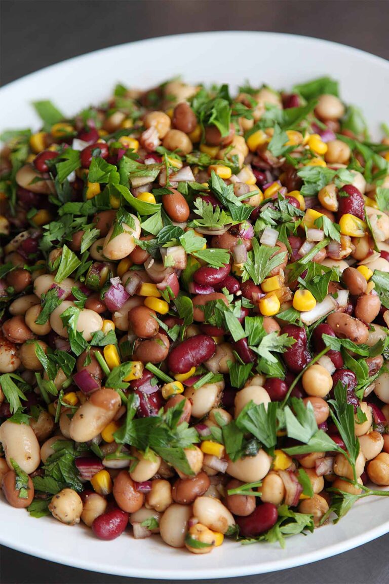 A dense bean salad with fresh herbs in a white bowl.